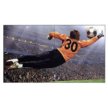 A Slim Bezel Video Wall displays a vivid image of a football goalkeeper in an orange jersey diving mid-air to stop the ball, set against the backdrop of a stadium packed with spectators.