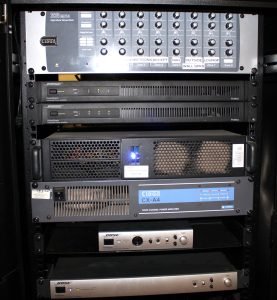 A rack with multiple audio equipment units, including amplifiers, mixers, and sound processors from brands like Cloud and Bose, each labelled with buttons, knobs, and indicator lights—just as you’d expect to find at Downhall Hotel in Essex.