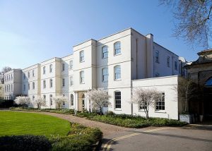 A large white building with three storeys, Sopwell House stands gracefully in St Albans, surrounded by small trees and a well-maintained lawn under a clear blue sky. Inside, guests can enjoy the stylish cocktail bar, perfect for relaxing or socialising after a day exploring the picturesque grounds.