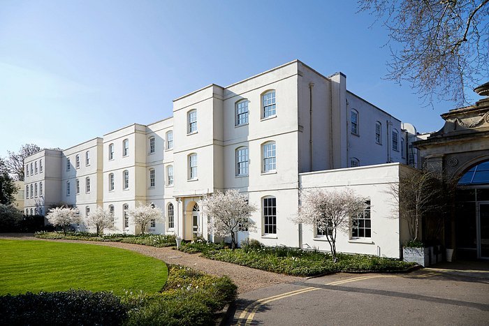 A large white building with three storeys, Sopwell House stands gracefully in St Albans, surrounded by small trees and a well-maintained lawn under a clear blue sky. Inside, guests can enjoy the stylish cocktail bar, perfect for relaxing or socialising after a day exploring the picturesque grounds.