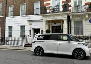 A white van with excite Group branding is parked on a quiet city street in front of classic brick and white buildings, not far from the elegant black iron railings and balconies of the Mayfair Islamic Centre.