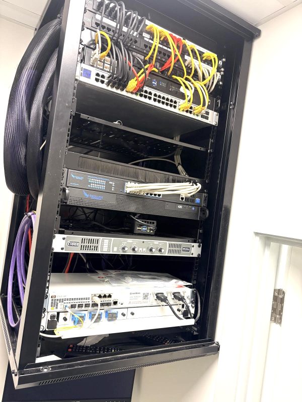 A network server rack with several switches, routers, and devices connected by yellow, red, and black Ethernet cables in a well-lit room at the ATIS Foods office in London.
