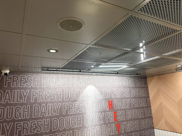 Ceiling with lights and sprinklers above a wall that repeatedly says DAILY FRESH DOUGH in white letters, with some letters highlighted in red to spell HEY vertically—a signature design element often seen at Domino’s Pizza locations, including the one in Hunstanton, where you can enjoy quick and convenient pizza delivery.