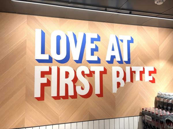 A wall in Hunstanton with large text reading LOVE AT FIRST BITE, featuring a bite mark taken out of the word BITE, and Domino’s Pizza fizzy drink bottles visible on the lower right.