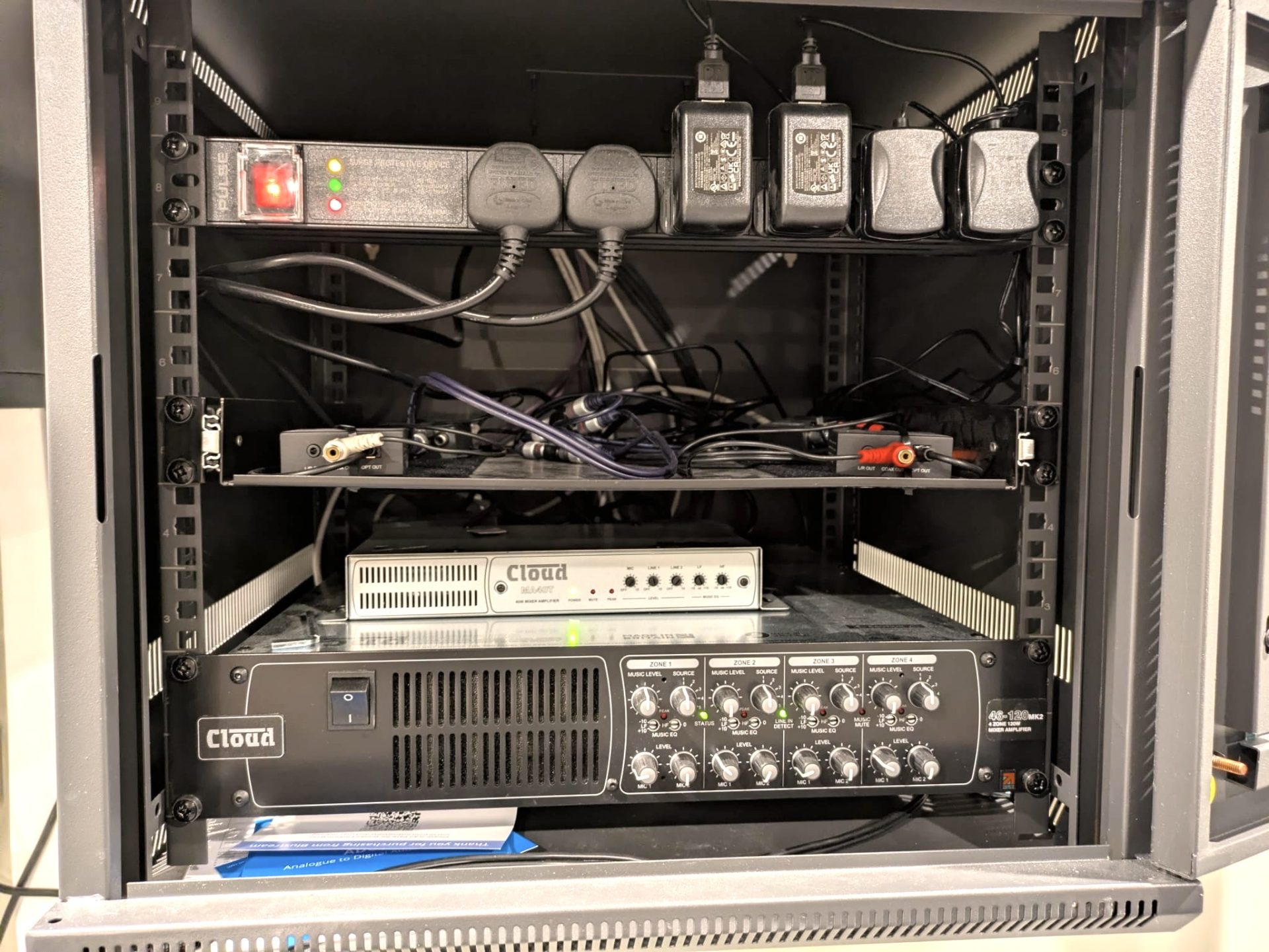 A rack-mounted audio equipment setup with power switches, cables, and two Cloud brand amplifiers or processors, organised on metal shelves inside an equipment cabinet—an ideal solution for professional AV installations in Edinburgh by Code Concepts.