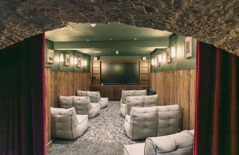 A cosy home theatre room with several cushioned seats facing a large flat-screen TV, wood-panelled walls, framed pictures, and soft lighting, viewed through an arched doorway—perfect for relaxing after exploring the historic streets of Edinburgh.