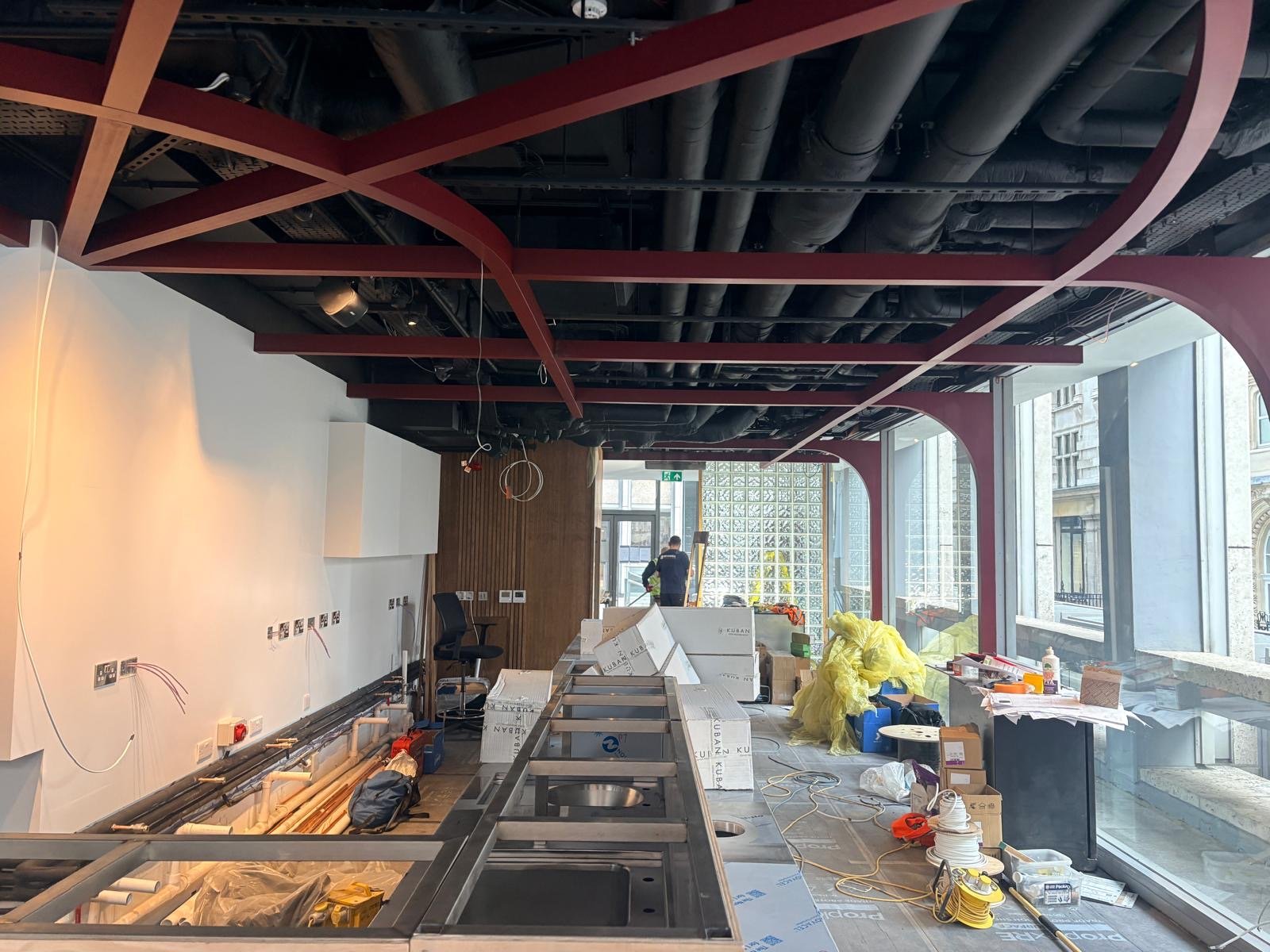 A modern indoor space under construction in London, with exposed pipes on the ceiling, scattered tools, building materials, and large windows letting in natural light—a future home for Guillam Coffee. A modern indoor space under construction in London, with exposed pipes on the ceiling, scattered tools, building materials, and large windows letting in natural light—a future home for Guillam Coffee.