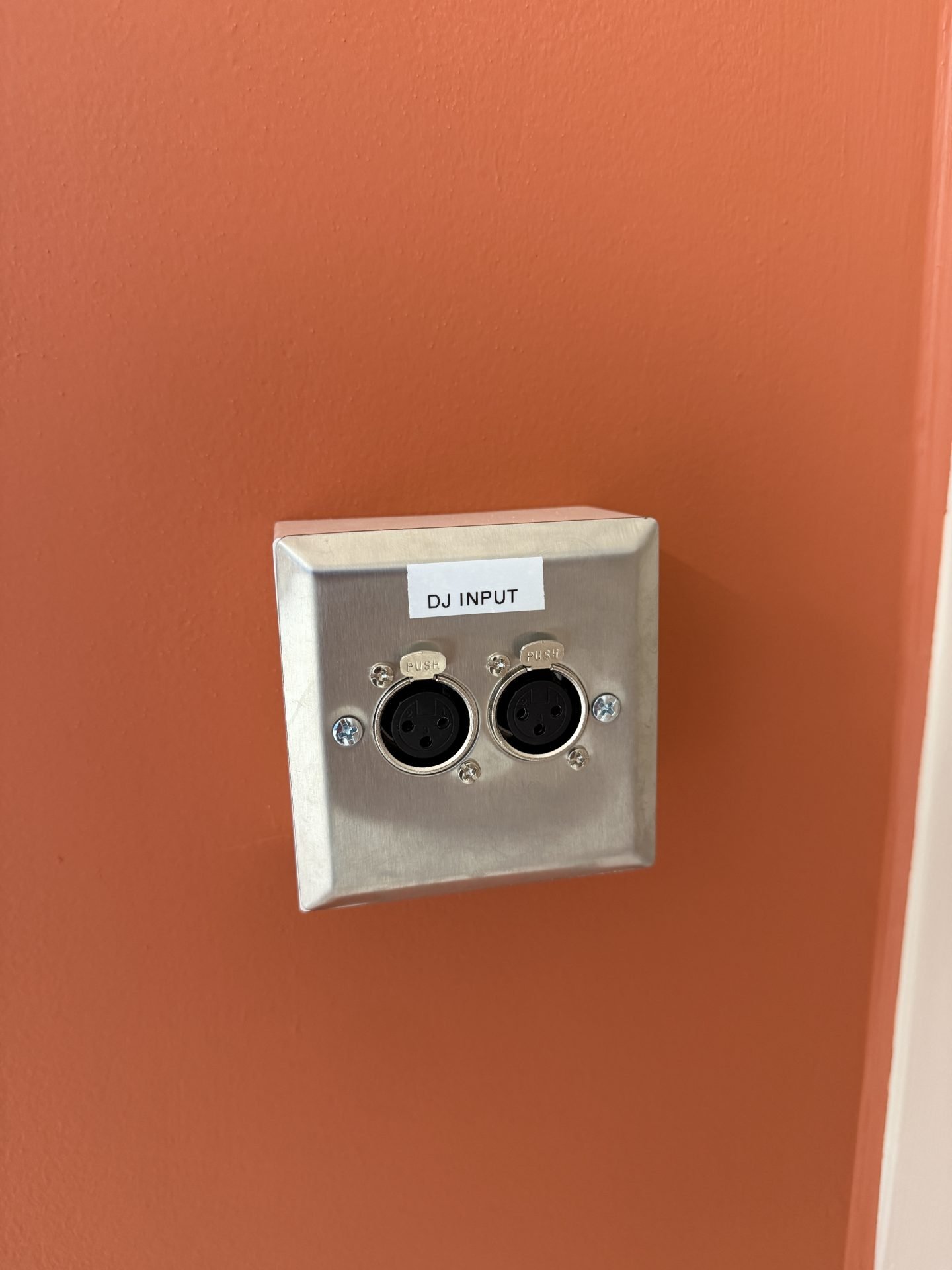 A metal wall plate with two XLR input ports labelled DJ INPUT is mounted on an orange wall in the Solt Room, Hackney, London.
