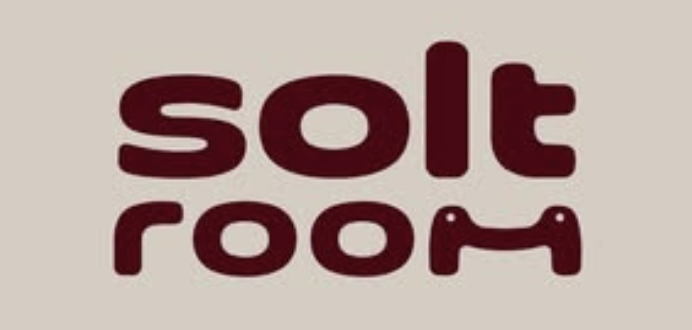 The image shows the words Solt Room in lowercase, stylised maroon font on a beige background. The “oo” in “room” resembles eyes, giving the letters a playful look. This distinctive design captures the welcoming vibe of Solt Room, a unique spot in Hackney, London.
