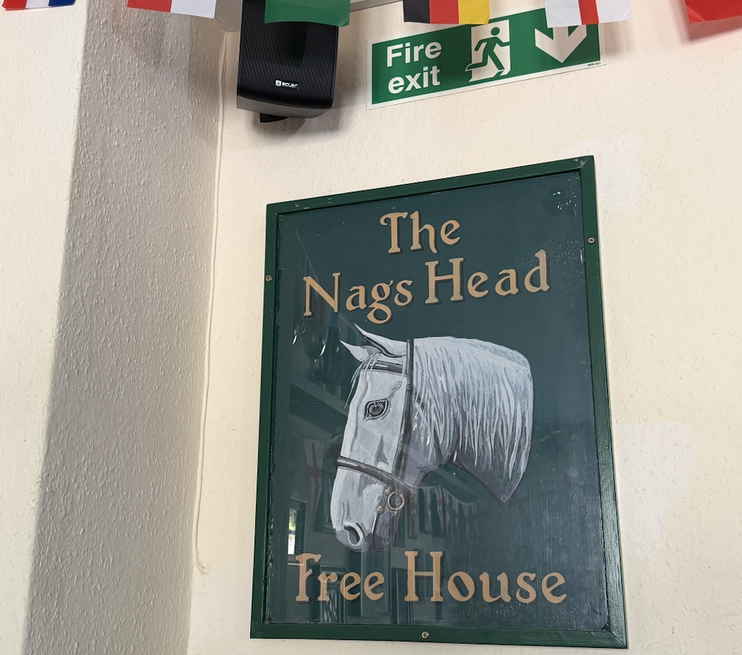 A sign with a white horse’s head and the text “The Nags Head Free House” hangs on a cream wall near a green fire exit sign, offering a welcoming sight for visitors exploring Lyme Regis. A sign with a white horse’s head and the text “The Nags Head Free House” hangs on a cream wall near a green fire exit sign, offering a welcoming sight for visitors exploring Lyme Regis.
